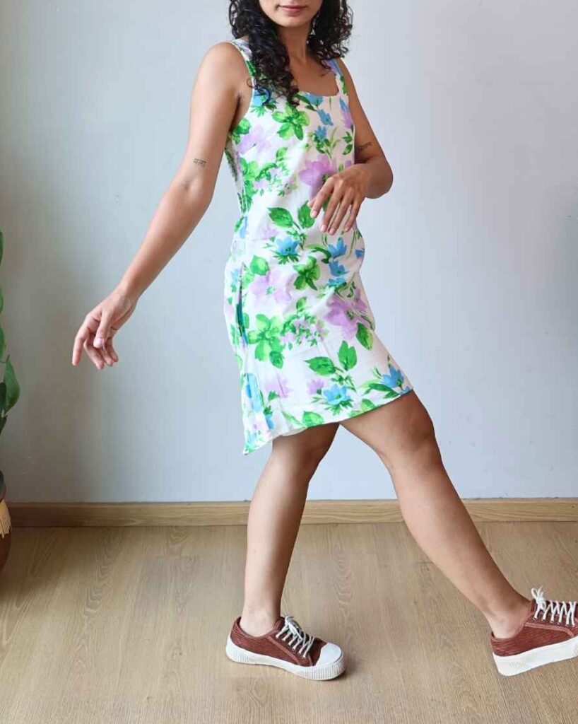 Woman walking in a white floral Pocket Dress with pink sandals, indoor plant in the background